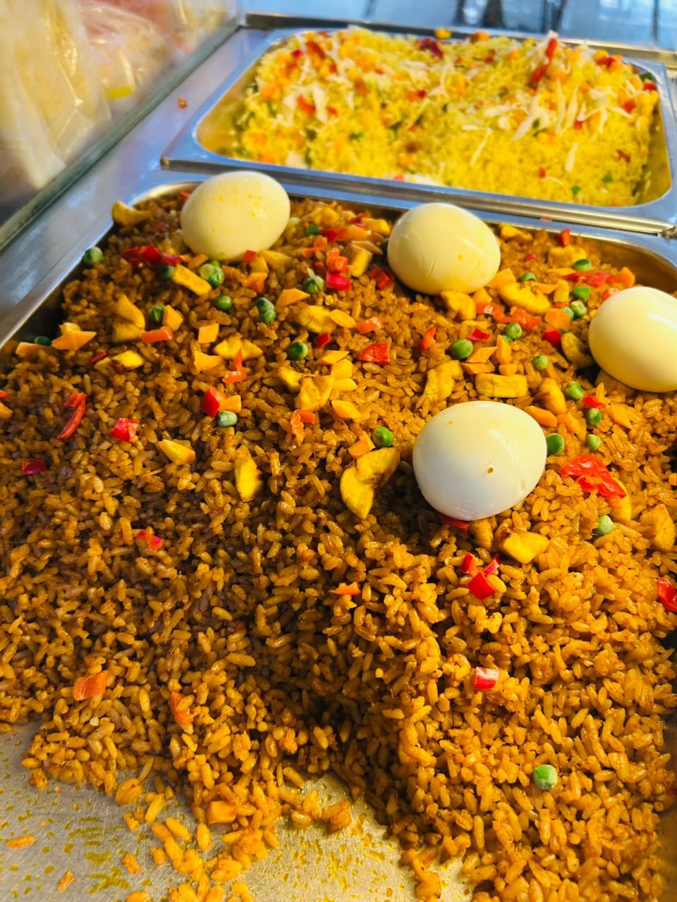 Trays of jollof rice with boiled eggs and fried rice